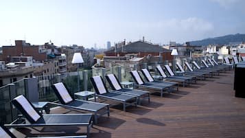 Terraza en la azotea con tumbonas y una cubierta de madera, con vistas a un paisaje urbano que incluye edificios y una colina distante.