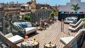 A rooftop terrace with wicker furniture, a wooden deck, and a city view. - Axel Hotel Barcelona - Adults Only (Barcelona)