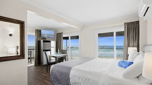 A hotel room with a large bed, a desk with a chair, a television, and a view of the beach. - Ocean Beach Hotel (San Diego)