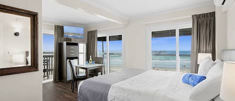 A hotel room with a large bed, a desk with a chair, a television, and a view of the beach.
