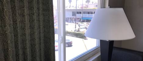 A room with a window, a lamp, and a view of a street with cars and buildings.