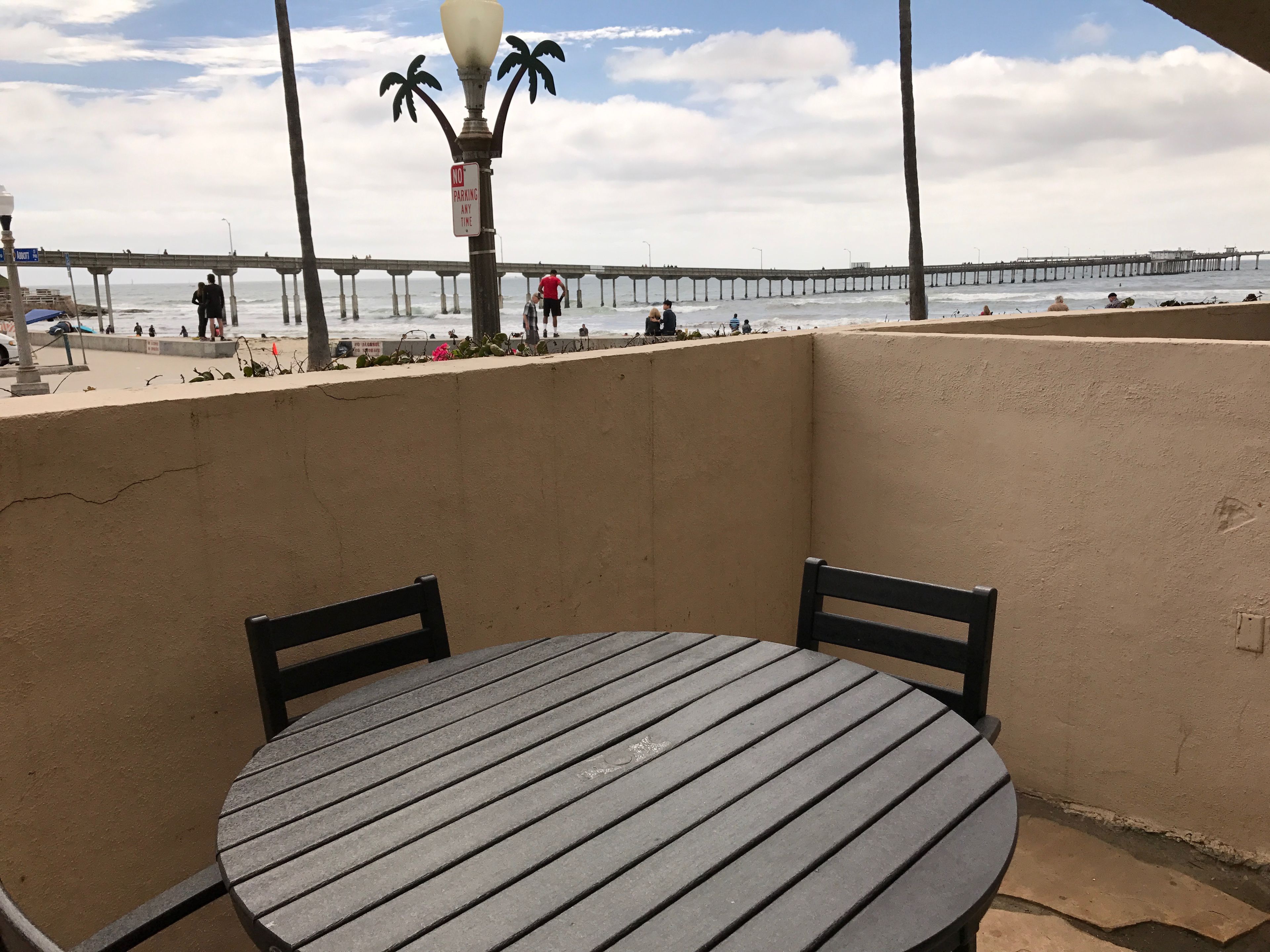 Un balcone con un tavolo rotondo e sedie, con vista su una spiaggia e un molo sullo sfondo.