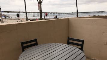 Un balcone con un tavolo rotondo e sedie, con vista su una spiaggia e un molo sullo sfondo.