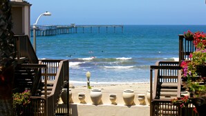 A beach view with a pier extending into the ocean, a staircase leading down to the beach, and a railing with potted plants. - Ocean Beach Hotel (San Diego)