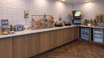 A breakfast buffet area with a variety of food items, a coffee station, and a refrigerated display.