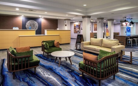 A hotel lobby with a reception desk, green armchairs, a beige sofa, and a coffee table.