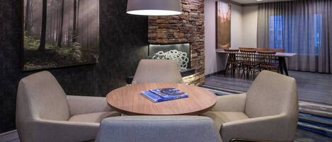 A conference room with a round table, two armchairs, a stone wall, and a large painting of a forest.