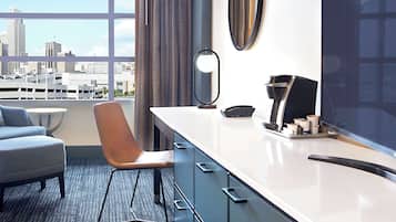 Habitación de hotel moderna con vista a la ciudad, un ventanal grande, un escritorio con cafetera y una silla.