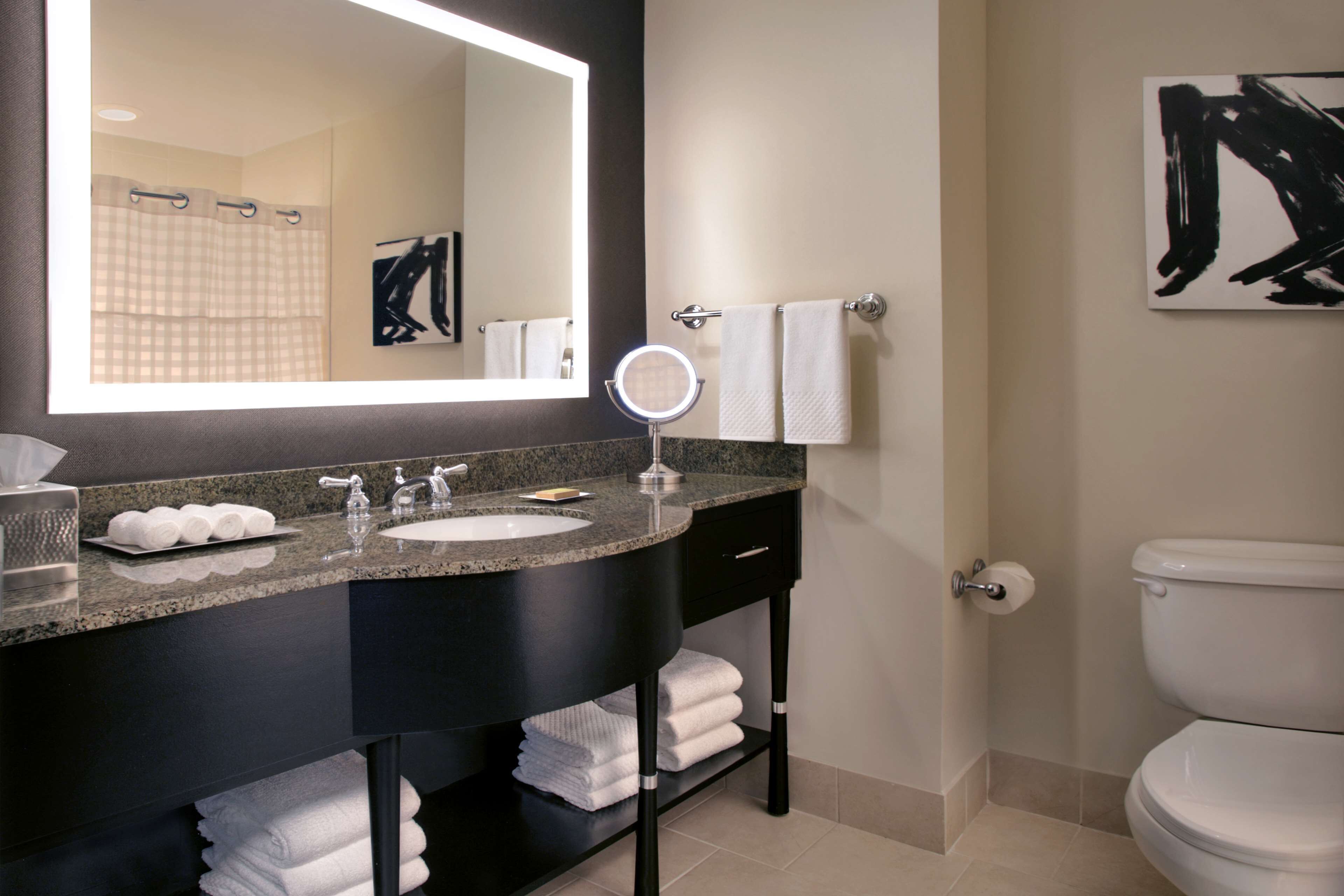 A modern bathroom with a granite countertop, a round mirror, a white sink, and a toilet.