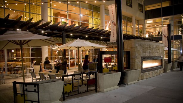 An outdoor dining area with tables and chairs, a stone fireplace, and umbrellas. - Hilton Omaha (Omaha)