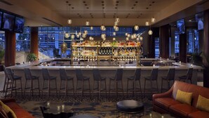 A bar area with a high bar counter, multiple seating options including bar stools and a sofa, and a large window offering a city view. - Hilton Omaha (Omaha)