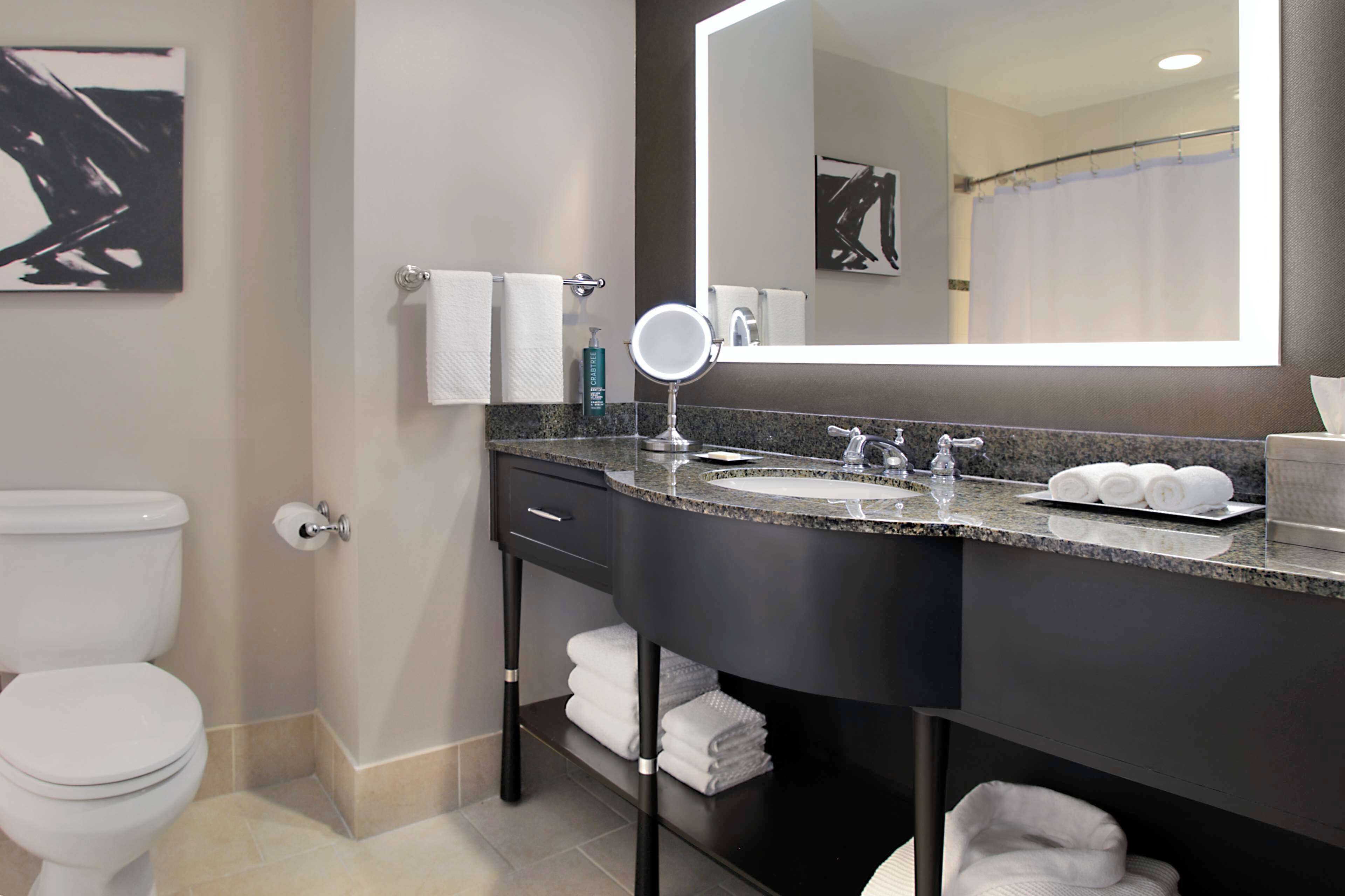 A modern bathroom with a white toilet, a sink with a mirror, and neatly folded towels on a shelf.
