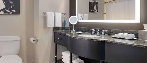 A modern bathroom with a white toilet, a sink with a mirror, and neatly folded towels on a shelf.