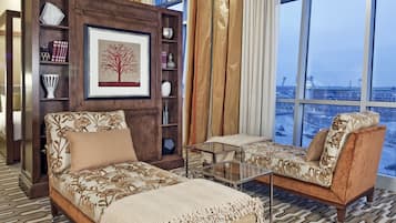 Ein geräumiges Hotelzimmer mit einem großen Bett, einem Sofa, einem kleinen Tisch und einem Bücherregal. Ein großes Fenster bietet Blick auf die Stadt.