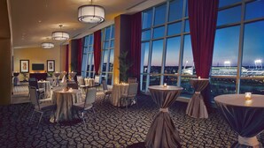 A hotel lobby with round tables, chairs, and large windows offering a city view. - Hilton Omaha (Omaha)