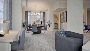 A modern living room with a grey sofa, a dining area with a table and chairs, and a kitchen in the background.