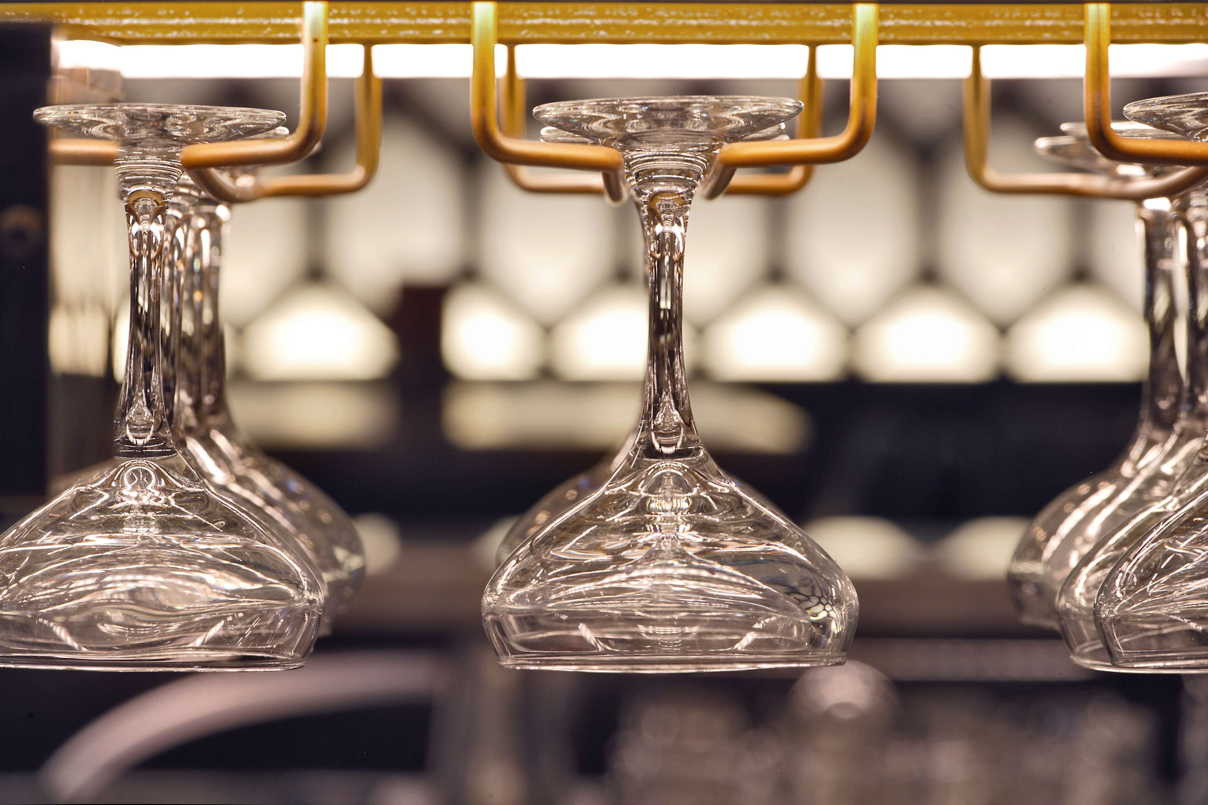 A row of clear glass wine glasses hanging from a golden bar structure.