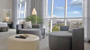 A modern hotel room with a large window, grey upholstered seating, a small table with a lamp, and a framed book on a ottoman. - Hilton Omaha (Omaha)