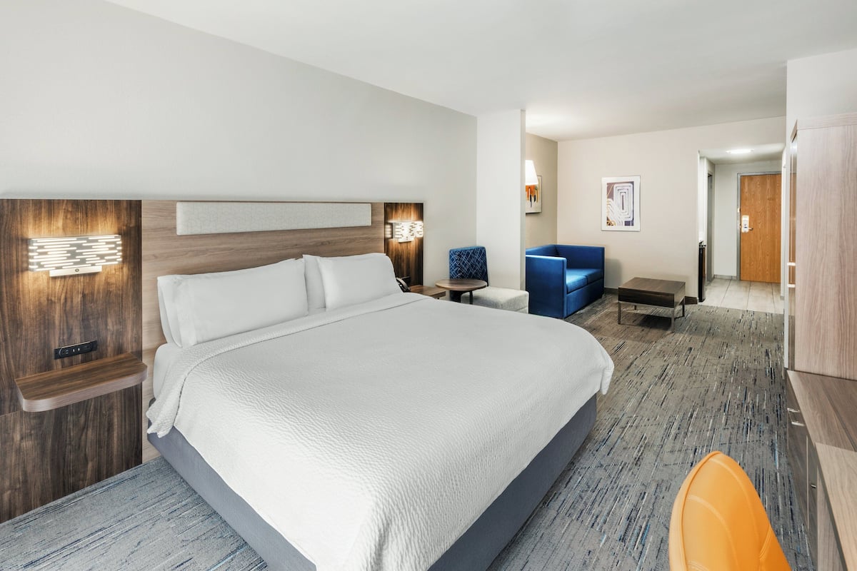 A hotel room with a large bed, bedside tables, a desk, a chair, and a wardrobe.