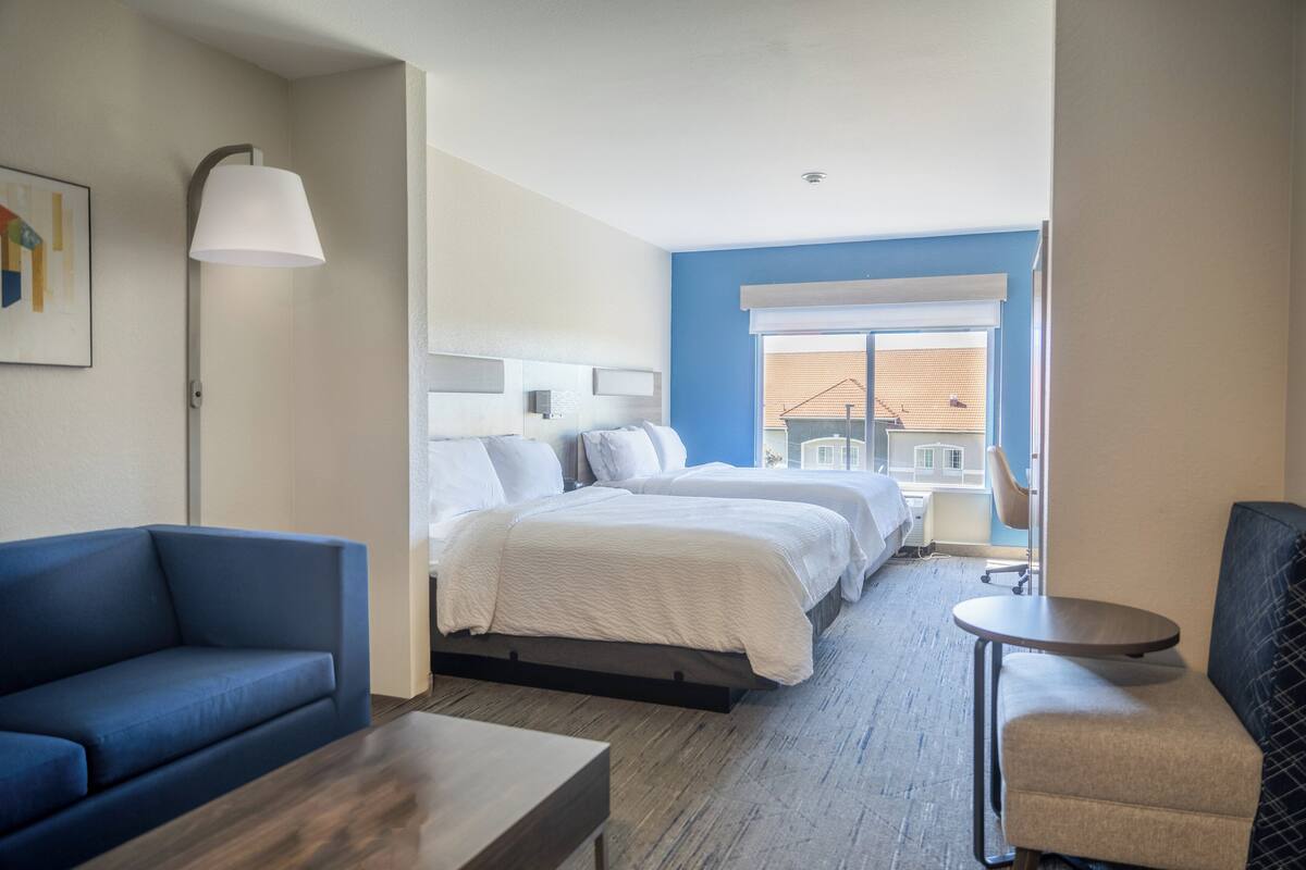 A hotel room with a bed, a blue sofa, a small table, and a chair.