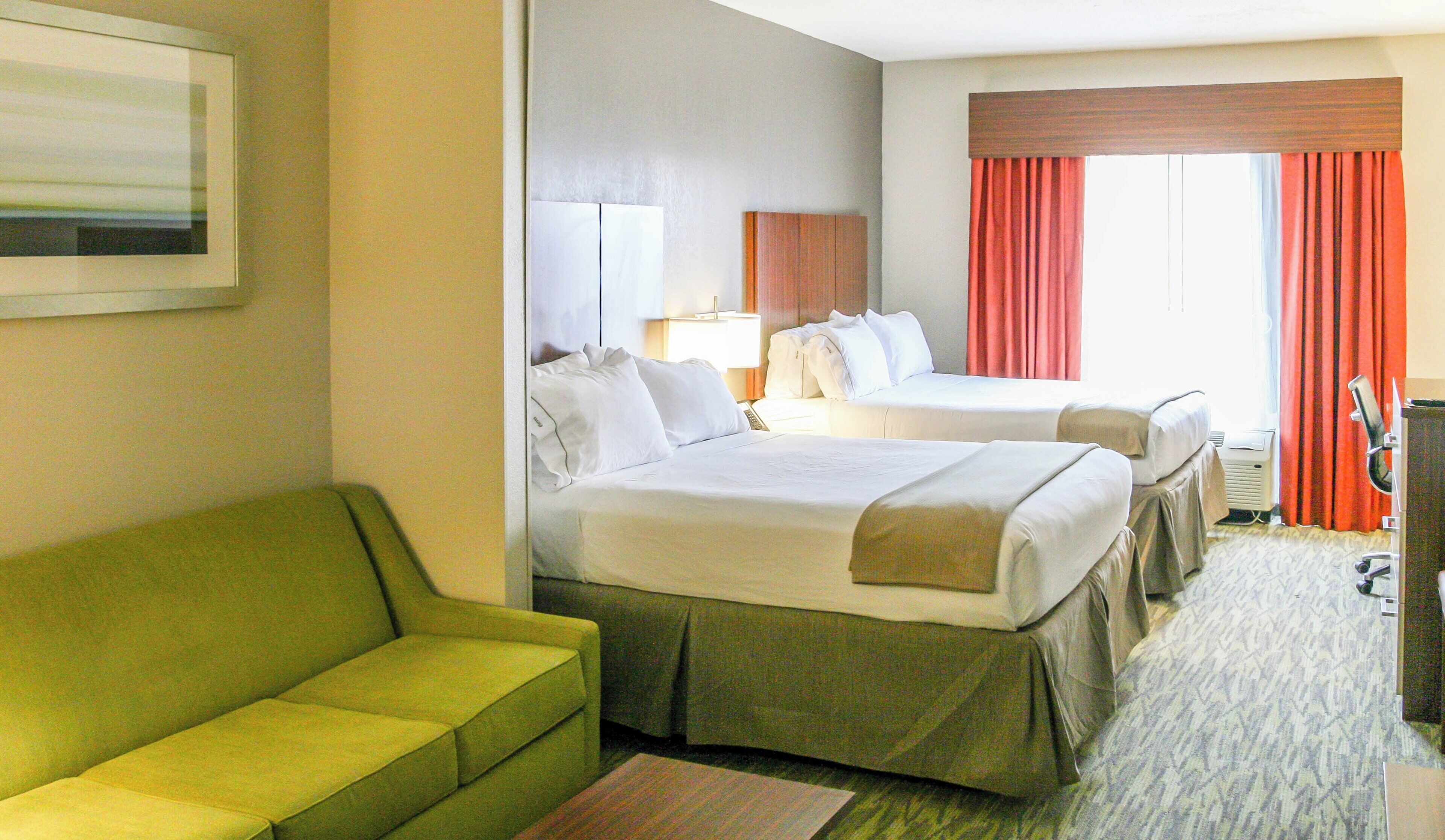 A hotel room with two beds, a green sofa, a desk with a lamp, and a painting on the wall.
