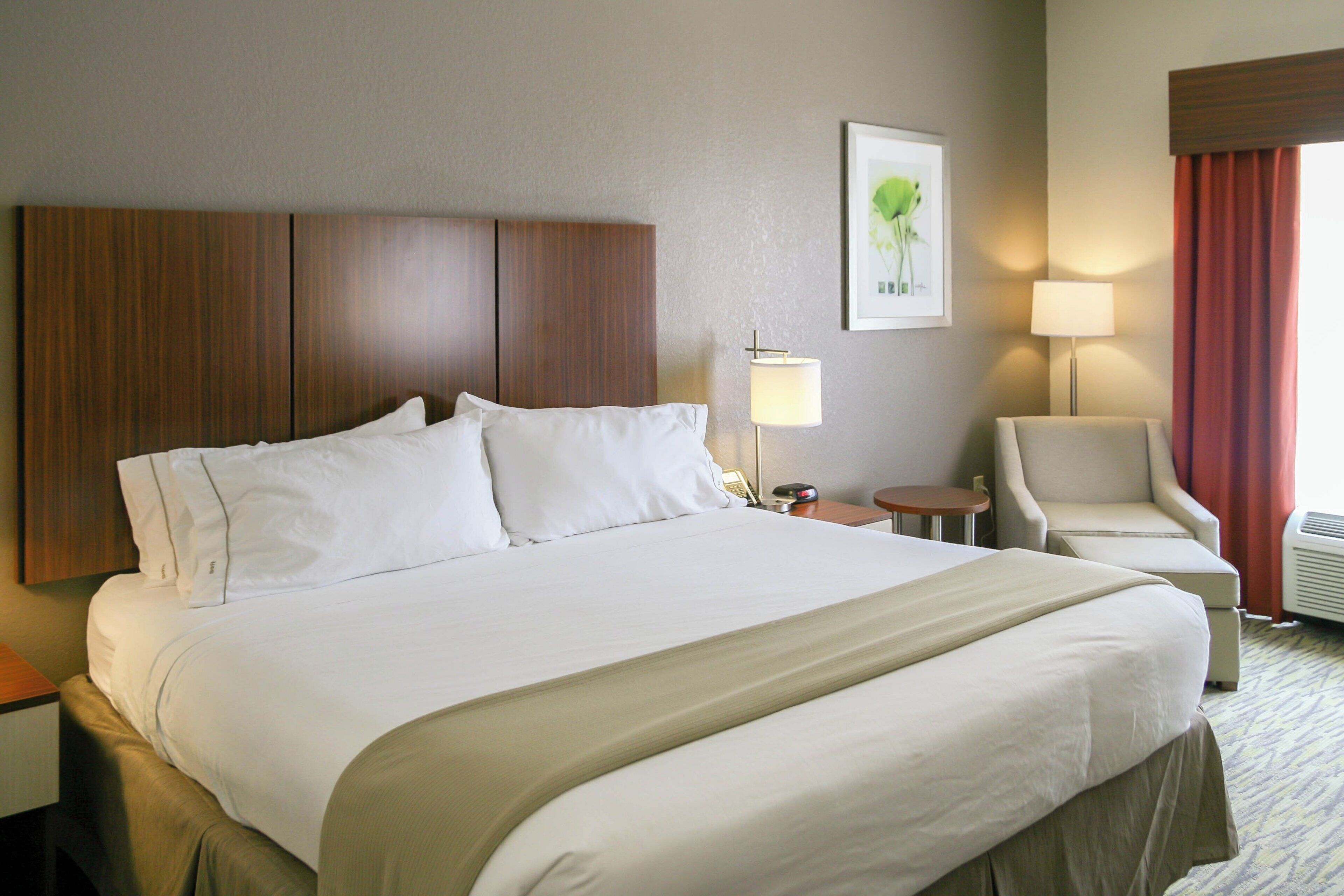 A hotel room with a large bed, a chair, a desk, a lamp, and a picture on the wall.