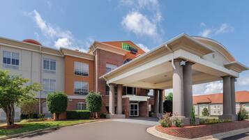 A Holiday Inn Express hotel with a covered entrance, brick facade, and a clear blue sky.