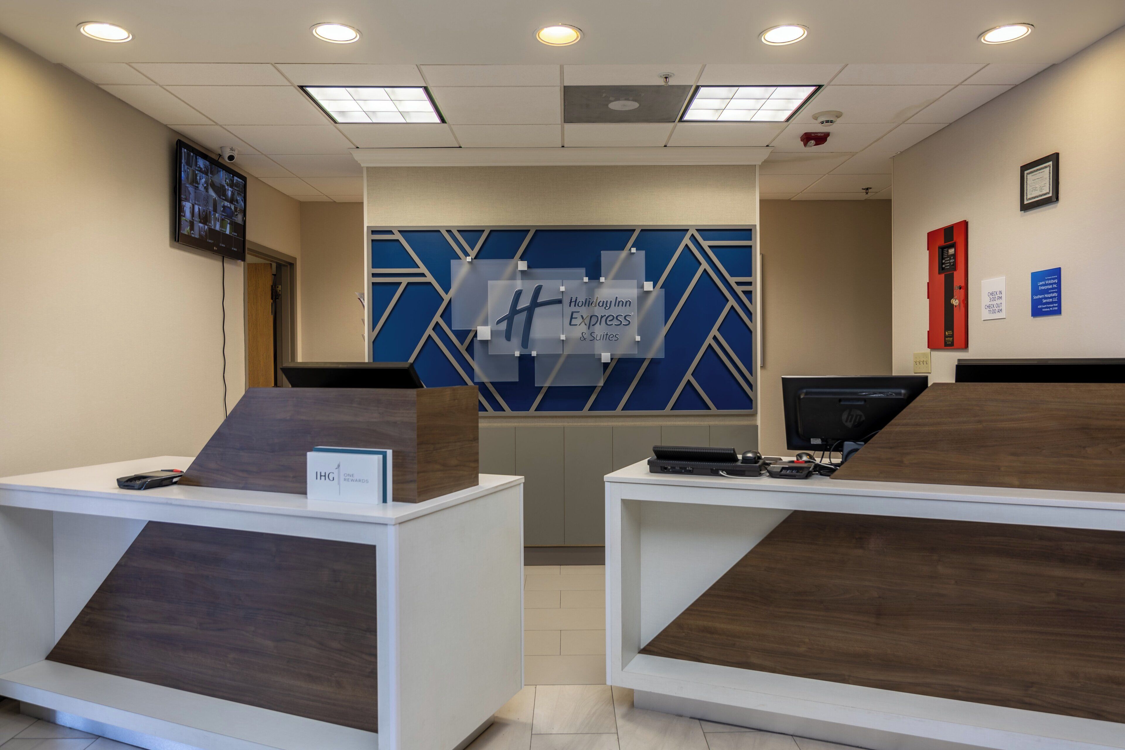 A reception area with a blue geometric wall design, two reception desks with nameplates, and a mounted television.