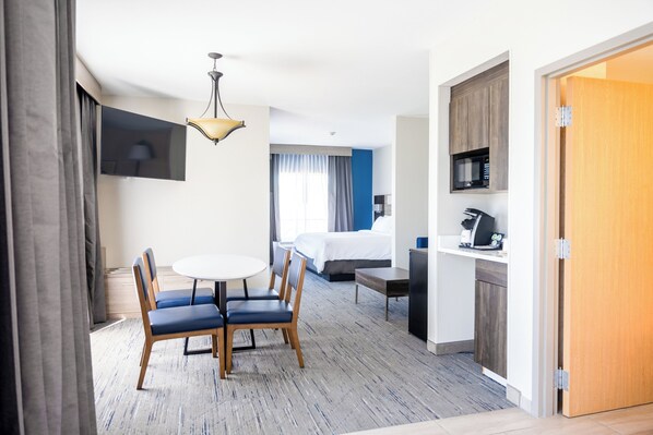 Een hotelkamer met een bed, een bureau met computer, een eettafel met stoelen, een aan de muur bevestigde televisie en een kitchenette.