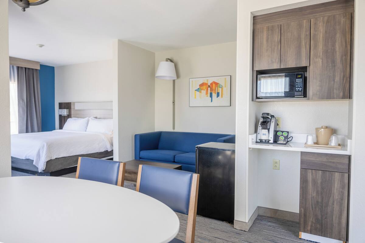 A hotel room with a bed, a blue sofa, a dining table, and a kitchenette with a microwave.
