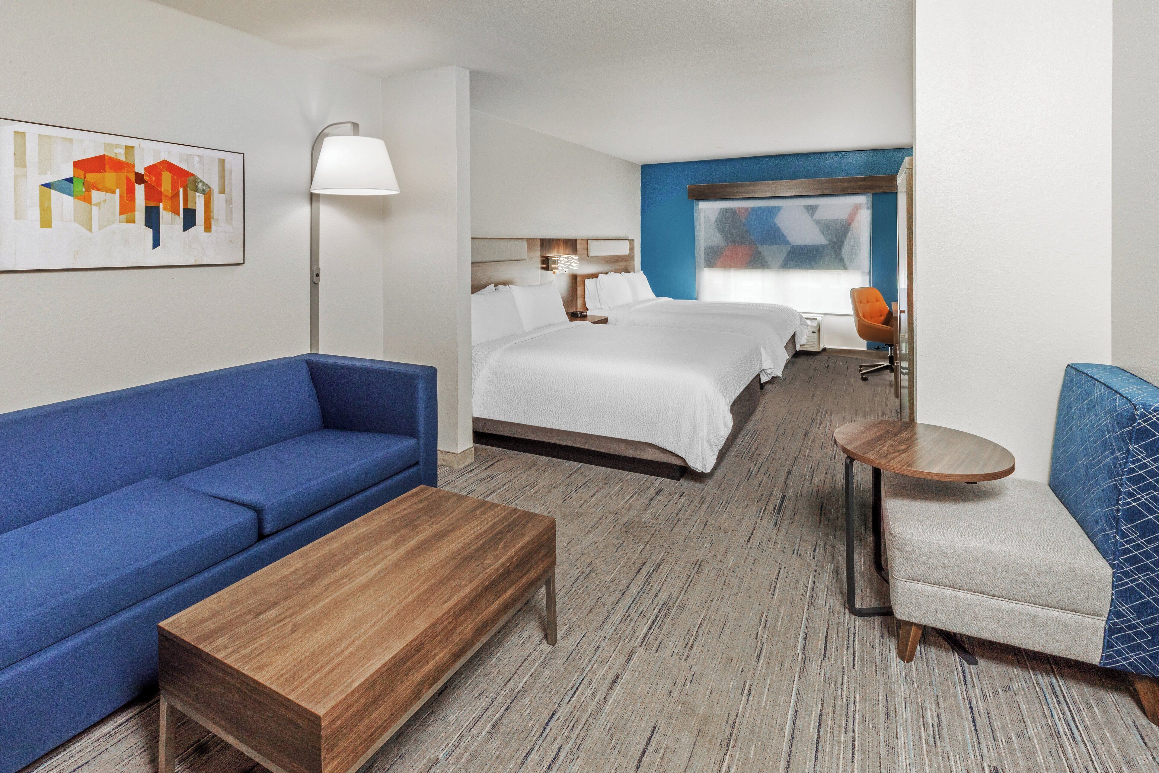 A hotel room with a large bed, a blue sofa, a wooden coffee table, and a small round table.