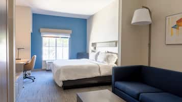A modern hotel room with a bed, a desk, a chair, a sofa, and a lamp.