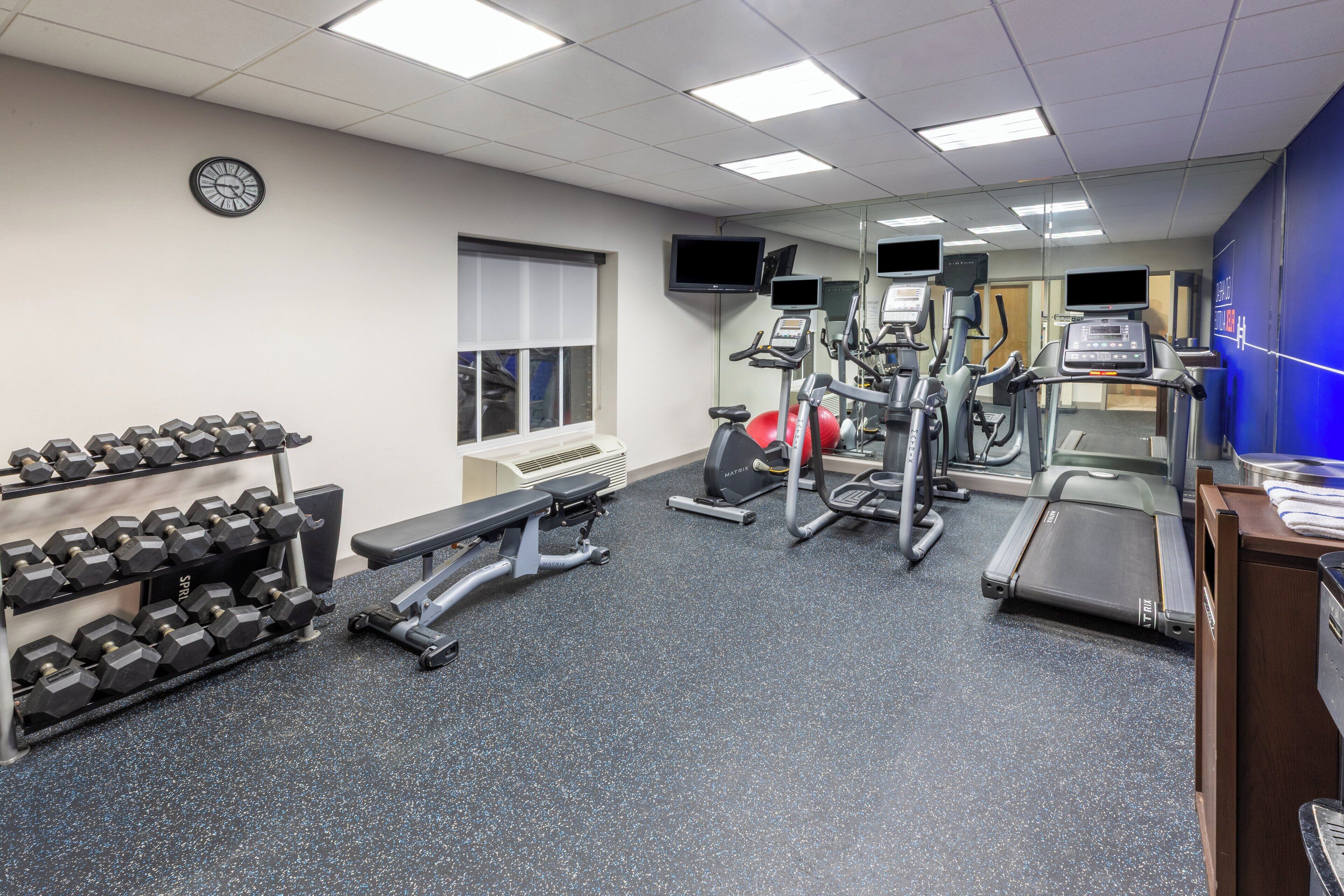 A gym with treadmills, elliptical machines, and dumbbells.