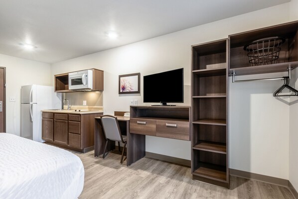 Una habitación de hotel compacta con kitchenette, una cama, un escritorio con computadora y un televisor.