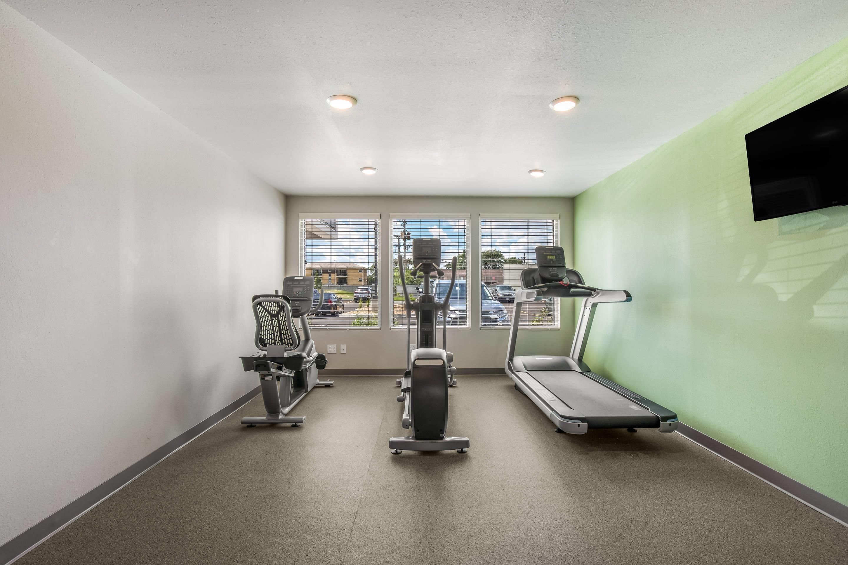 Un gimnasio con cintas de correr, elíptica y bicicleta estática, con vistas a coches aparcados afuera.