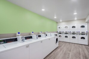 Un moderno lavadero con varias lavadoras y secadoras, un panel de control y una pared verde.