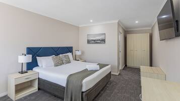 A hotel room with a bed, bedside tables, a flat-screen TV, a wardrobe, and a carpeted floor.