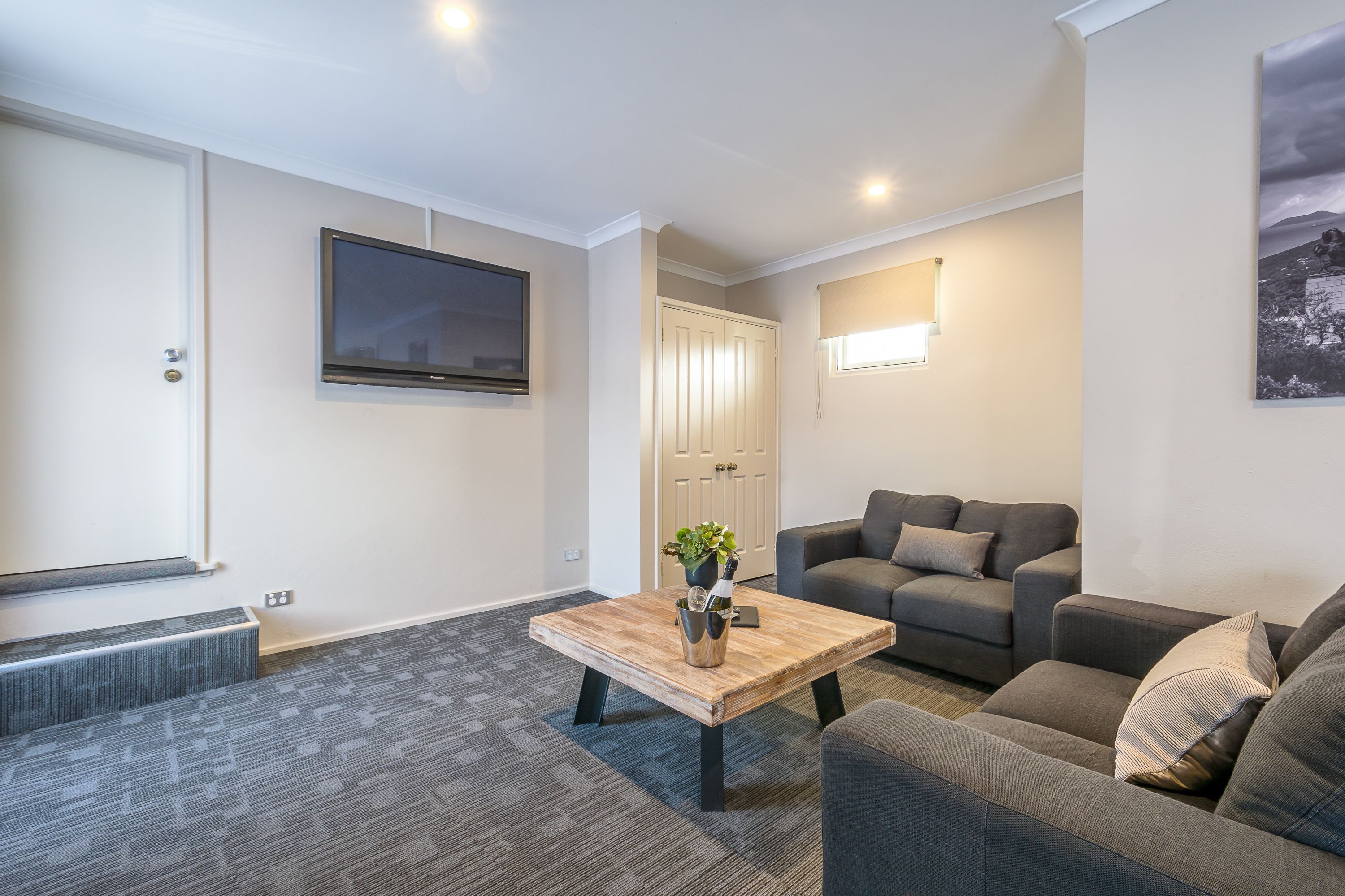 A modern living room with a grey sofa set, a wooden coffee table, and a flat-screen TV mounted on the wall.
