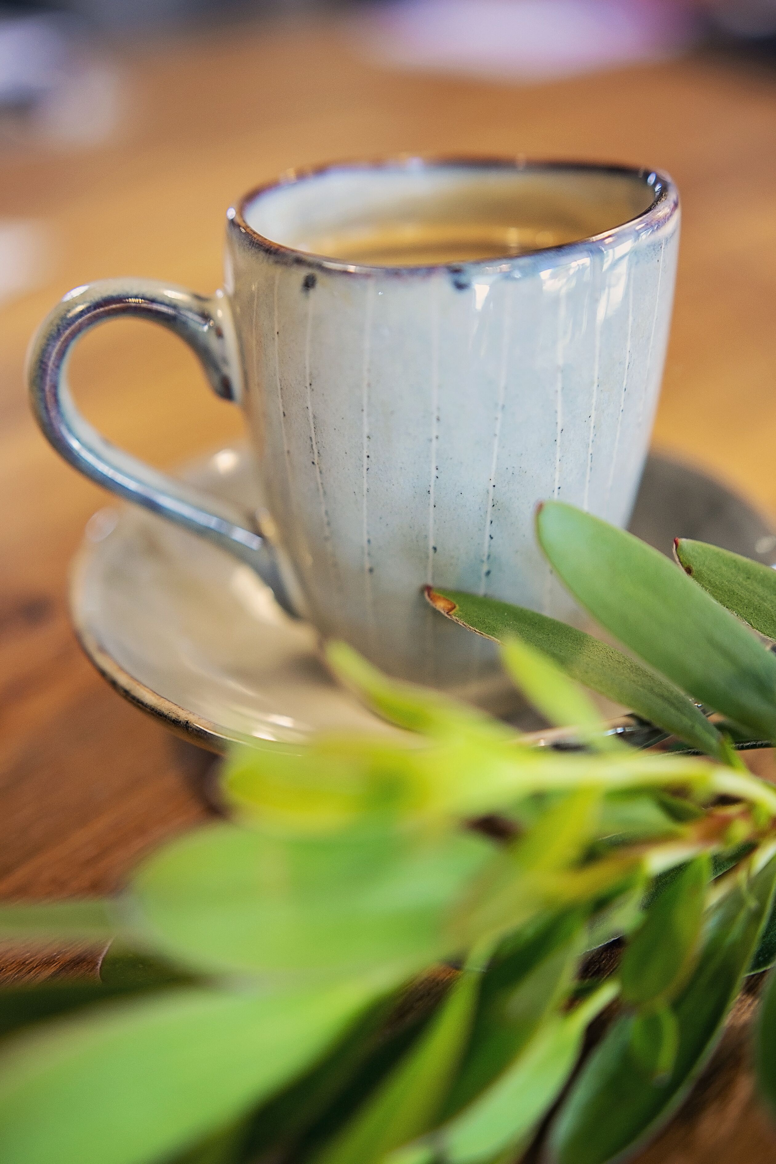 A ceramic mug with a handle on a saucer, placed on a wooden surface.