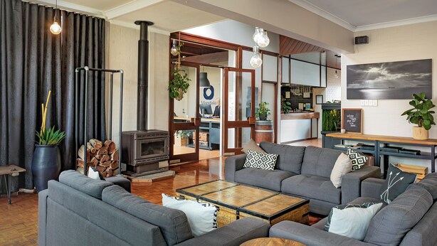 A modern living room with a fireplace, grey sofas, a coffee table, and a large window. - Mandala Ace Albany Hotel (Centennial Park)