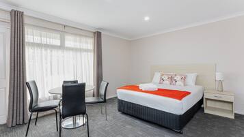 Een hotelkamer met een bed, nachtkastje, stoel, klein tafeltje en een raam met gordijnen.
