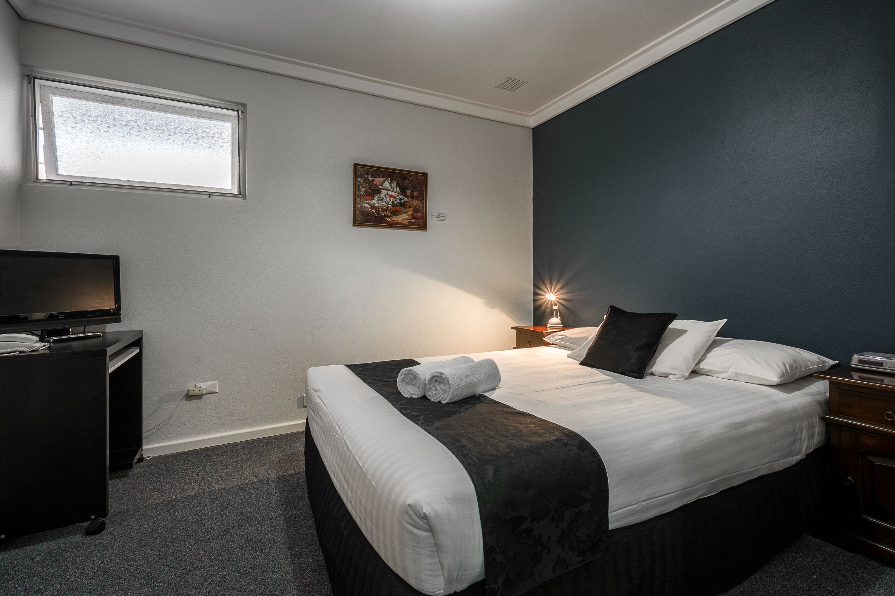 Una habitación de hotel con una cama, televisión, un cuadro en la pared y una ventana.
