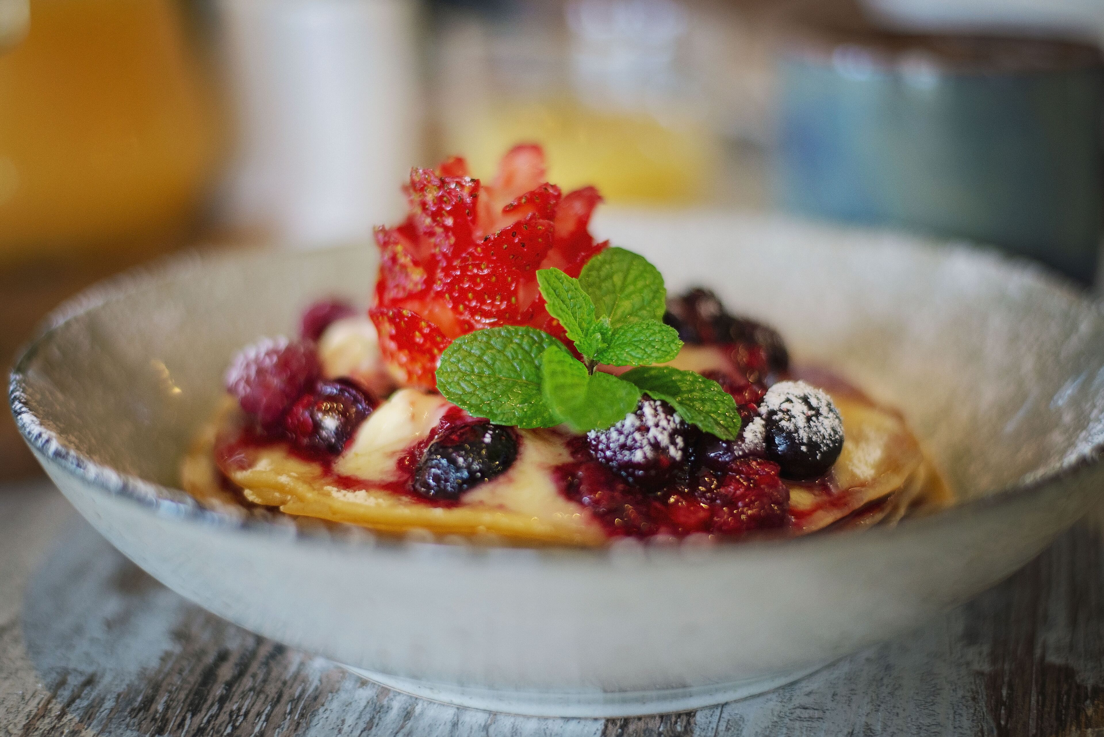 A dessert with berries and mint on a ceramic plate.