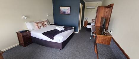 A hotel room with a bed, a desk, a chair, a wardrobe, a painting on the wall, and a hallway.