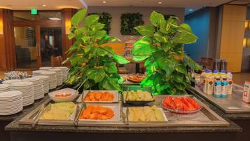 Buffet com diversas frutas e legumes, pratos empilhados à esquerda e um bar de sucos à direita.