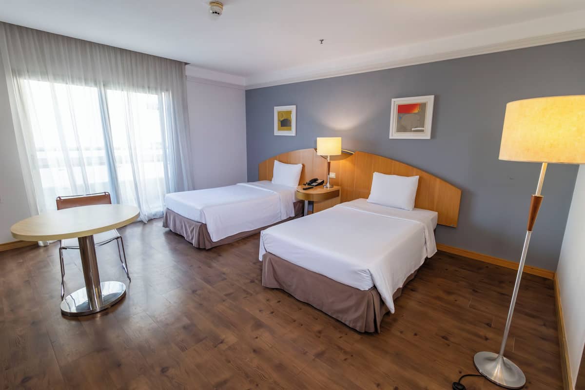 Hotellihuone, jossa on kaksi sänkyä, pyöreä ruokapöytä, lamppu ja tuoli.