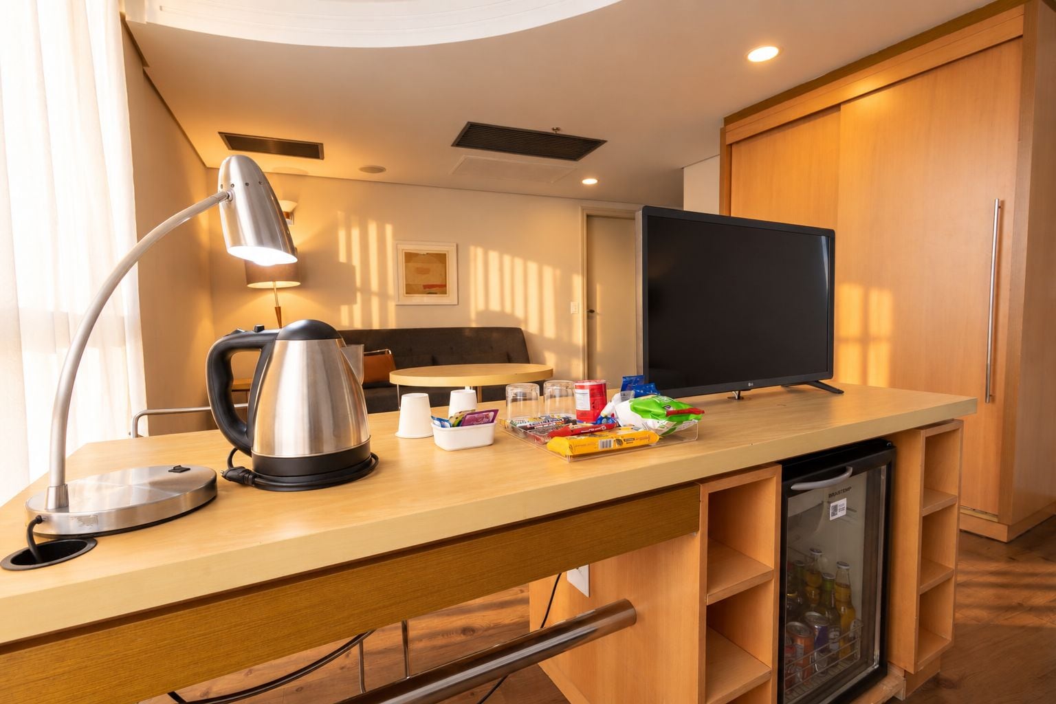 Une chambre d’hôtel équipée d’un bureau, d’une bouilloire, d’une lampe, d’une télévision et d’un mini-bar.