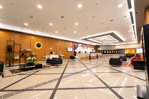 Een moderne hotel lobby met een receptiebalie, een zithoek en een grote wand met kunstwerken.