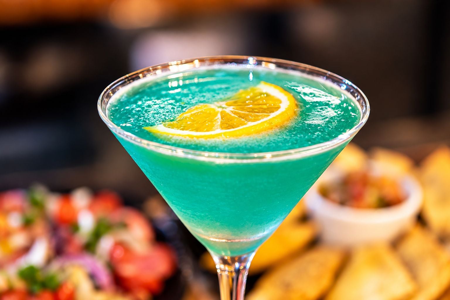 Un cóctel en una copa de martini con una rodaja de naranja en el borde.