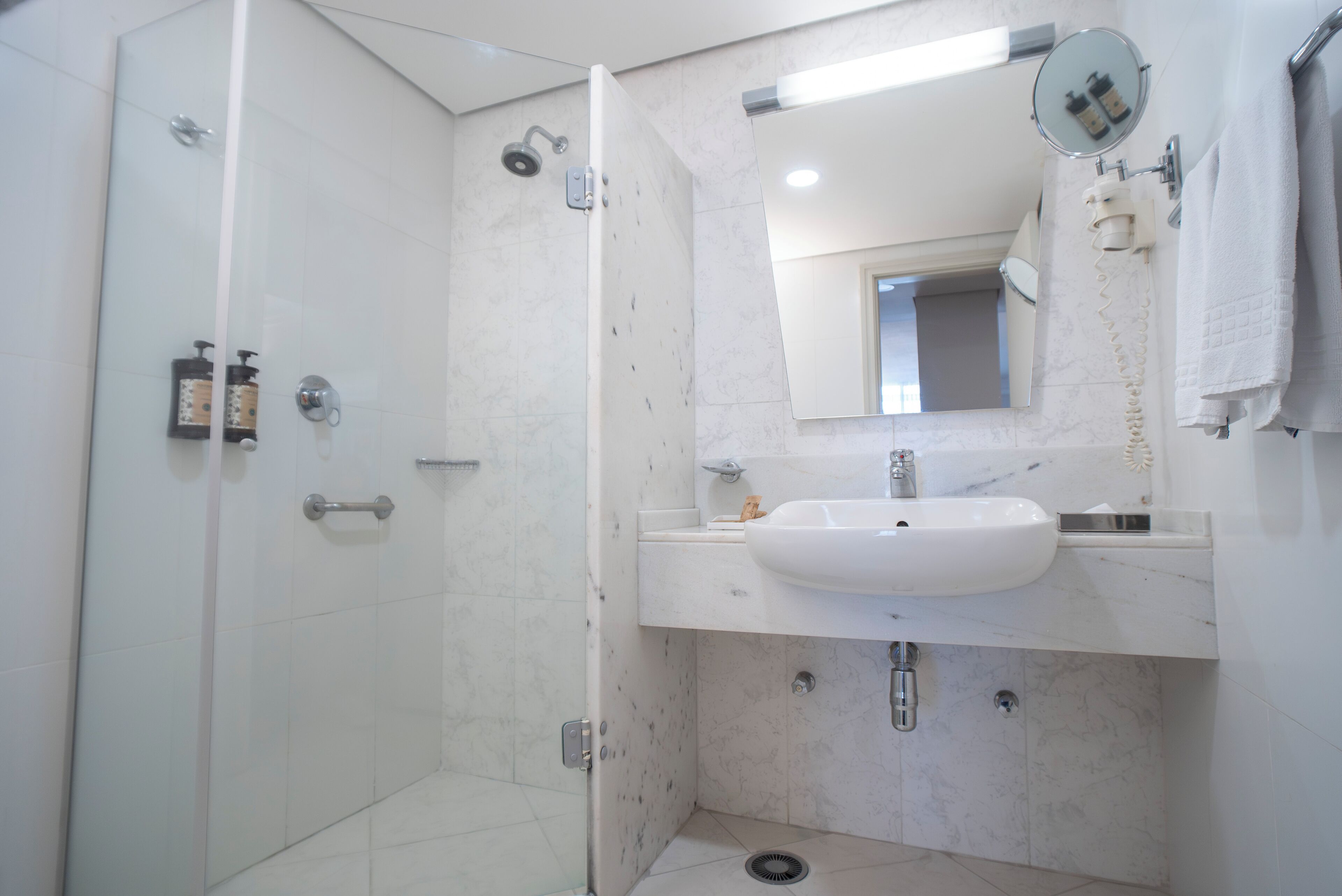 Un baño moderno con ducha de vidrio, lavamanos blanco y espejo sobre el lavamanos.